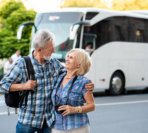 Happy senior couple of tourists hugging in front of tourist bus
